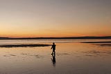 A gorgeous sunset on a beach with a child walking in it.