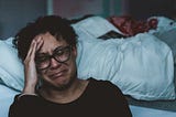 A woman crying on the side of her bed.