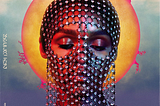 The face of Janelle Monae, a Black woman, with her eyes closed. She wears a piece of chainmail draped over her face and a sun is painted behind her head as a halo. The painting blends the style of religious art and sci-fi/fantasy imagery. The album title “Dirty Computer” is on the left side.