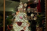 Flower shop window display featuring a white Christmas tree decorated in red and pink for Valentine’s Day.