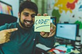 Smiling man showing sticky note with code illustration.