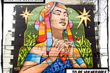 A colorful photo of an illustration on a building in Lima, Peru. The picture depicts a beautiful woman holding her heart between her hands. The caption reads, “Have the courage to be vulnerable.”