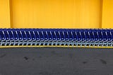 A row of blue shopping carts in front of a yellow wall.