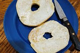 A picture of sliced bagel with cream cheese spread on a blue plate with a small knife