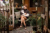 A woman sitting in a busy room cuddling a cat.