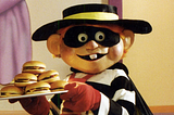 the Hamburglar is a costumed mascot of McDonald’s, wearing a hat, face mask, cape, striped top, and red gloves