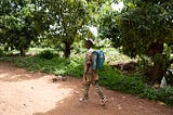 A young learner carrying a backpack walks on an unpaved road