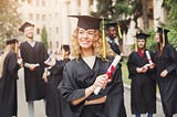 Blonde woman holds diploma. Wears grad attire.