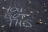 You Got This written in chalk on asphalt with small leaves scattered around.