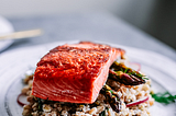 A white plate filled with farro, topped with roasted asparagus with seasoned salmon on top