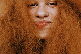 Black woman with big red hair, smiling at camera