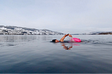 Female swimming front crawl in lake with snow on the surrounding hills.