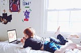 Brothers laying on a bed watching a laptop.