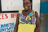 A pregnant woman wearing a yellow dress smiles outside of the door to the clinic. The sign behind her reads: Services Offered: OPD, Antenatal, Immunization, HIV Counseling.