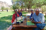 Author and smiling others seated at table at an oasis in the Namib desert
