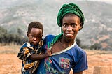 An African mother with her child in hand. They’re both on a dry land.