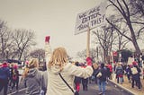 Woman holding a sign that reads “We are better than this.”