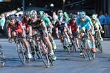 Competing bicyclists cooperate to form a peloton. Photo by Quino Al on Unsplash. Image shows a dozen bicyclists riding close together.