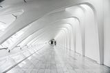 Black and white hallway with arched ceilings, tiled flooring and a door at the end. The door feels far away, it is very small in the photo.