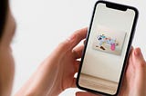 A woman holds a phone. She’s trying out a piece of art on her walls using Augmented Reality, and seeing how it would look if she bought it.