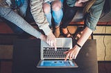 Three people excitedly pointing at a laptop screen