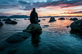 man sitting on a rock in still water. be here in the now