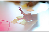 Photograph showing a person using a smart phone in a meeting room with others present.