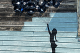 Picture of a bunch of old 33 rpm records nailed to a wall, to look like balloons, with string attached to each and bundled to the bottom, of a silhoutte of a girl painted on the wall, which looks like the balloons are carrying the girl away.