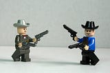 Fotos de dois personagens de Lego. Estão vestindo roupas típicas do velho oeste americano e segurando duas armas de brinquedo