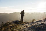 Solo Travel — Man standing atop a hill overlooking the landscape (https://unsplash.com/@capturethemoment)