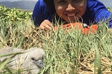 Smiling person in blue shirt lays on grass next to seabird chick.