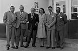 The cast of “The Jack Benny Program,” standing in a line outside the doors of NBC studios. Jack Benny has his arms linked with Don Wilson and Mary Livingstone