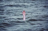 Photo of a hand reaching up out of the blue sea, as if someone is drowning.