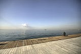 solitary man sitting on long wooden dock fishing