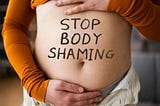 A woman’s stomach with the words, ‘stop body shaming’ written across