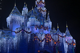 Night shot of Sleeping Beauty Castle at the Disneyland Resort decorated for the holidays with white icicle lights, multi-color lit garland, and a wreath.