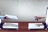 Dwie osoby przekazujące sobie dokument przez ekrany laptopów — symboliczne przedstawienie tematu jak napisać podanie o pracę i przesłać je online.