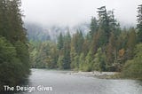 A person sits by a wide river surrounded by trees on very cloudy day in Washington State.