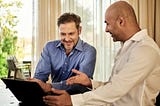 Two men talking while looking at a laptop. Photo by Docusign on Unsplash