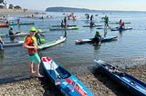 Ivan standing on shore at the start of the race next to paddleboards, surfskis, and outrigger canoes