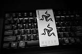 A sheet of Razer’s famous stickers sitting on top of a powered-on Keychron V1 gaming keyboard. The top two stickers depict the Razer snake logo and the bottom one is just their name. The photo is in black and white.