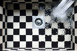 Water going down the drain in a black-and-white tiled shower.