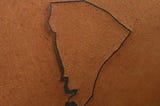 A line-drawing tattoo in black ink, shaped like a distorted inverted triangle, on brown skin