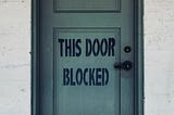Old door that says “This door is blocked.”