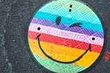 Smiley face drawn in colors of the rainbow on sewer drain
