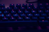 A keyboard bathed in purple light with glowing letters in pink on keys.