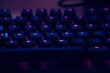 A keyboard bathed in purple light with glowing letters in pink on keys.