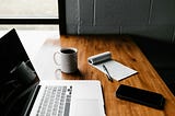 laptop, white ceramic mug, and black smartphone on table