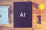 A black box labeled AI on a desk with glasses, a small statue and an e-notebook.