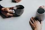 Two sets of hands holding coffee cups implying a man and woman in conversation